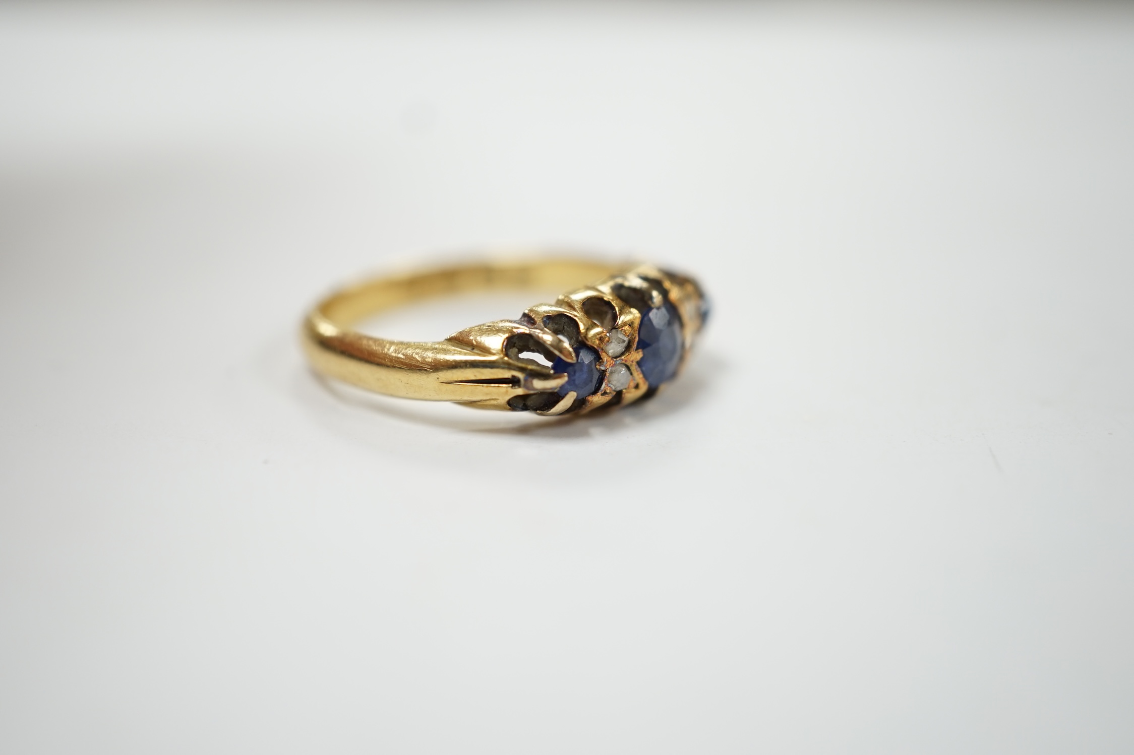 An early 20th century continental yellow metal (stamped 18) and three stone diamond set half hoop ring, with four stone diamond chip spacers, size O, gross weight 4.5 grams. Fair condition.